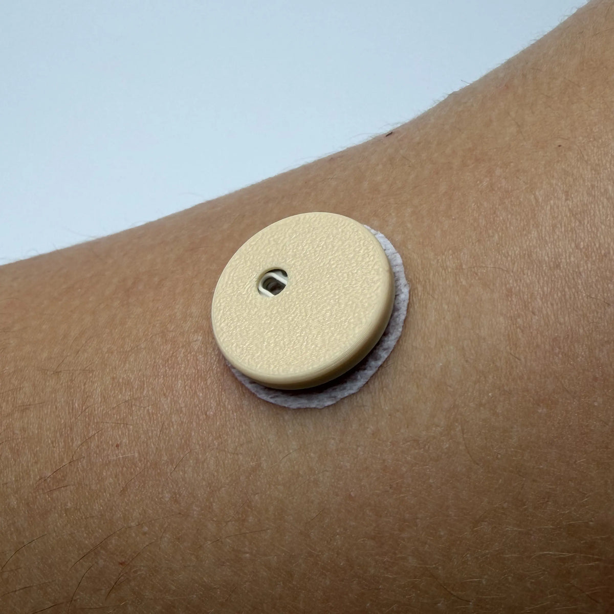 Coque beige clair sur un capteur FreeStyle Libre 3 porté au bras, en gros plan